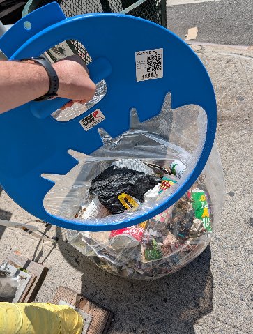 An overflowing public trash can on the sidewalk, full of litter