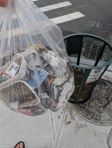 A bag stuffed full of collected litter next to a public trash can